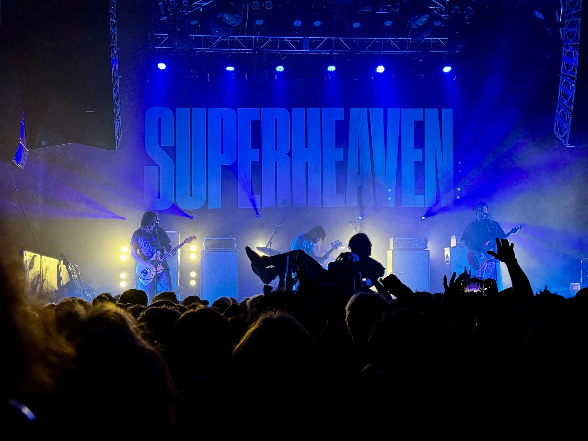 Superheaven on a blue-lit stage, with a crowd surfer riding over the crowd.